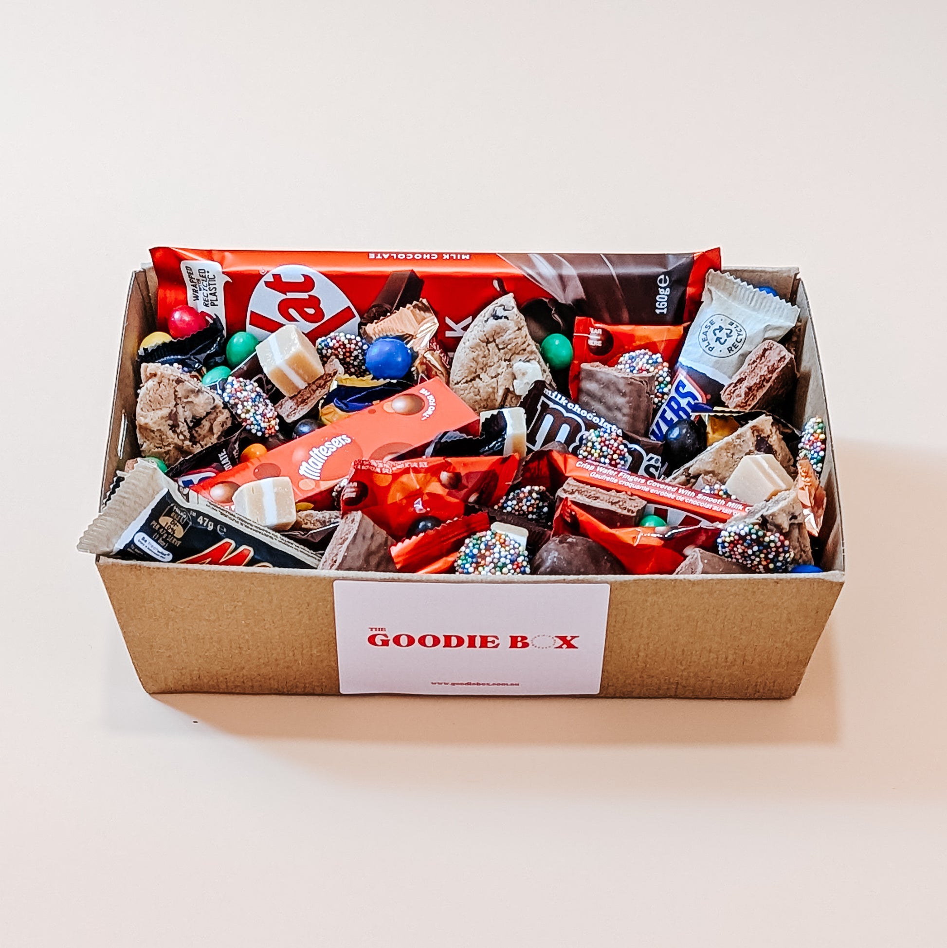 Photograph close-up photograph of a chocolate dessert box filled with a variety of chocolates, including large Kit Kat, Maltesers, Twix, M&M's, and rich fudge