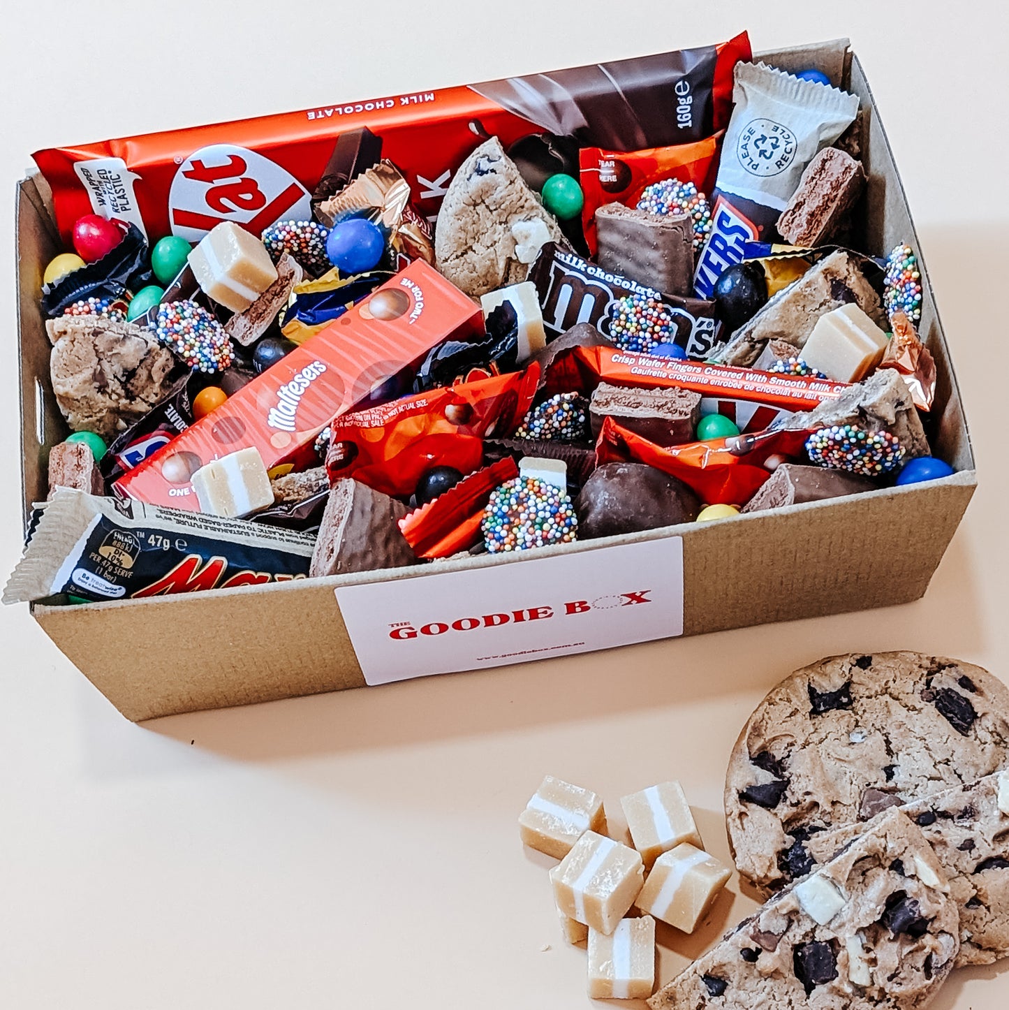 Photograph of a chocolate dessert box featuring an assortment of treats including Kit Kat, Maltesers, Twix, M&M's, and creamy fudge.