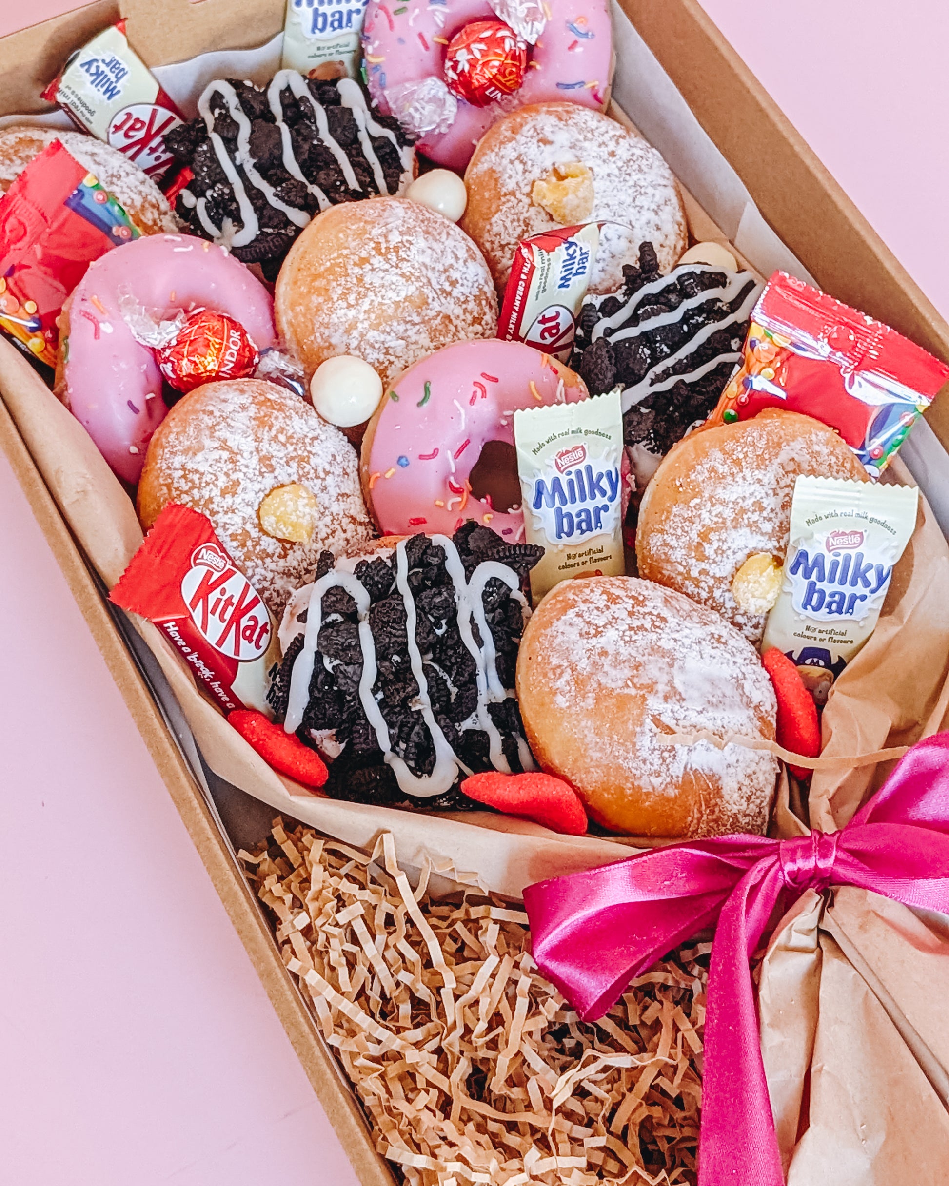 Close up photograph of a box of donuts arranged in a bouquet style. The box also contains an assortment of fun size chocolates and lollies.