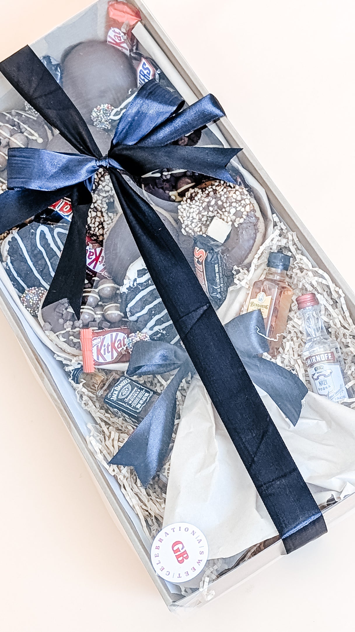 Photography of donut bouquet dessert box for him. The box is filled with twelve donuts of different flavours including chocolate oreo, chocolate and cream, chocolate malteser and hazelnut. It also has an assortment of loose chocolates and lollies and 4 x minature alcohols. Wrapped with a silk black bow.