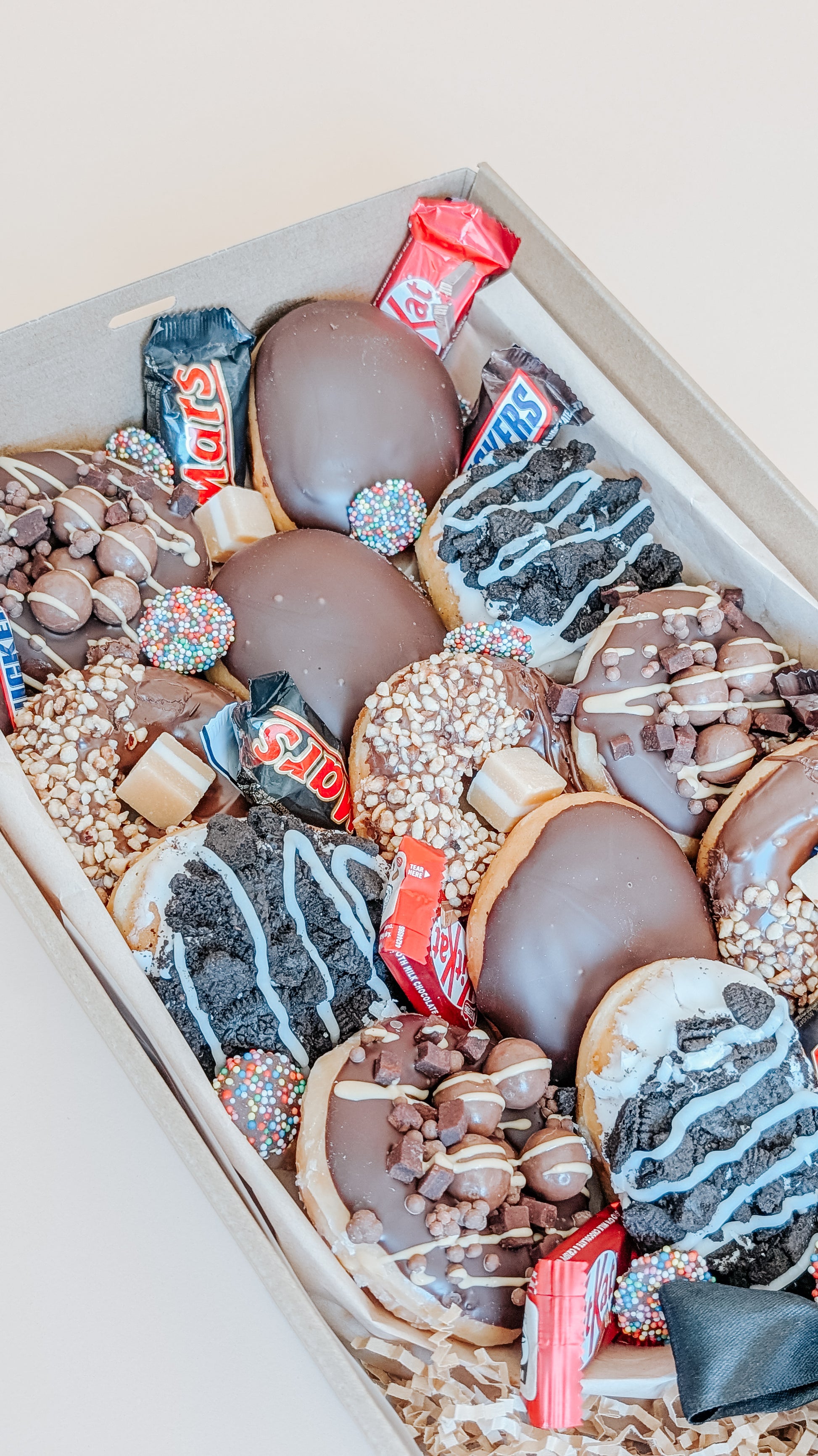 Photograph of a box of donuts arranged in a bouquet style close up. The box also contains an assortment of fun size chocolates and lollies.