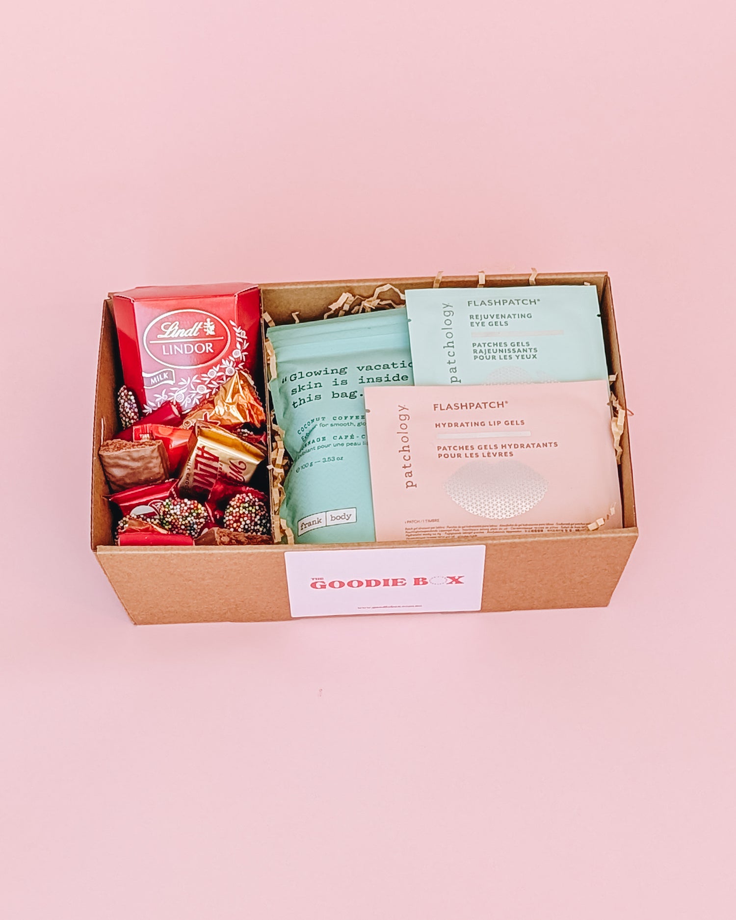 Photograph of pamper hamper. The box is filled with pampering goods such as Frank Body scrub, eye mask and lip mask and contains an assortment of sweet treats.