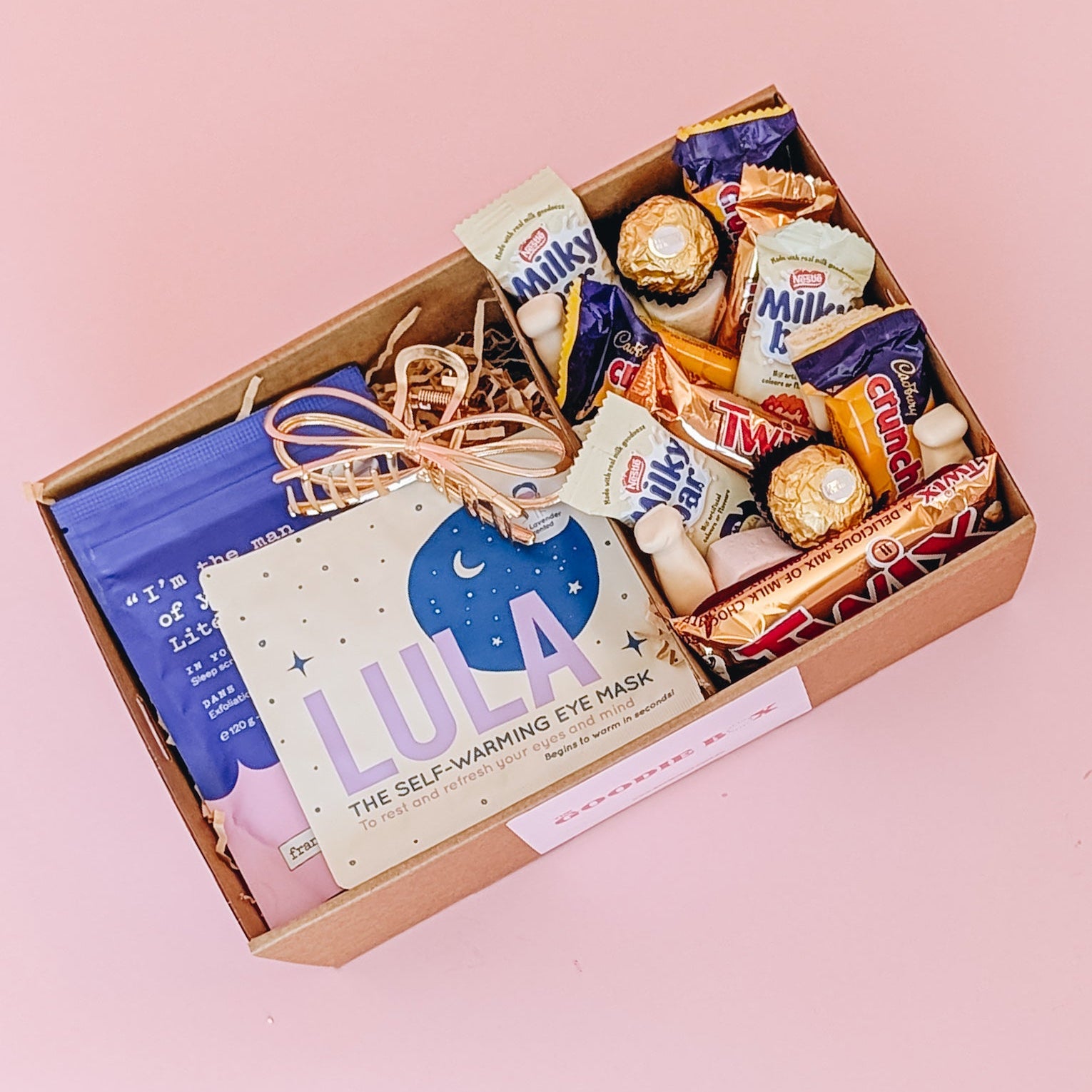 Photograph of pamper hamper sleepy time filled with gold hair claw, frank body scrub, Lula self warming eye mask and a selection of sweet treats, including marshmallows, Crunchie, Milky Bar, Twix & Ferrero Rocher.
