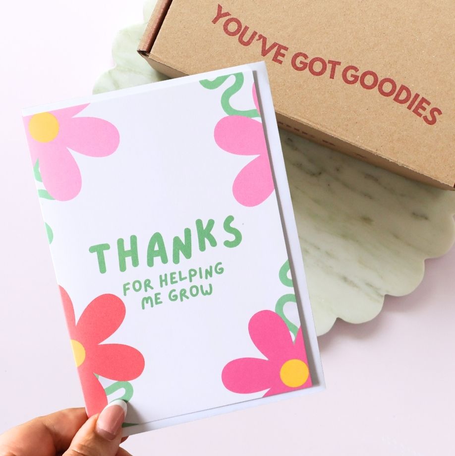 Floral card with 'THANKS FOR HELPING ME GROW' text held by a hand, with a box labeled 'YOU'VE GOT GOODIES' in the background.