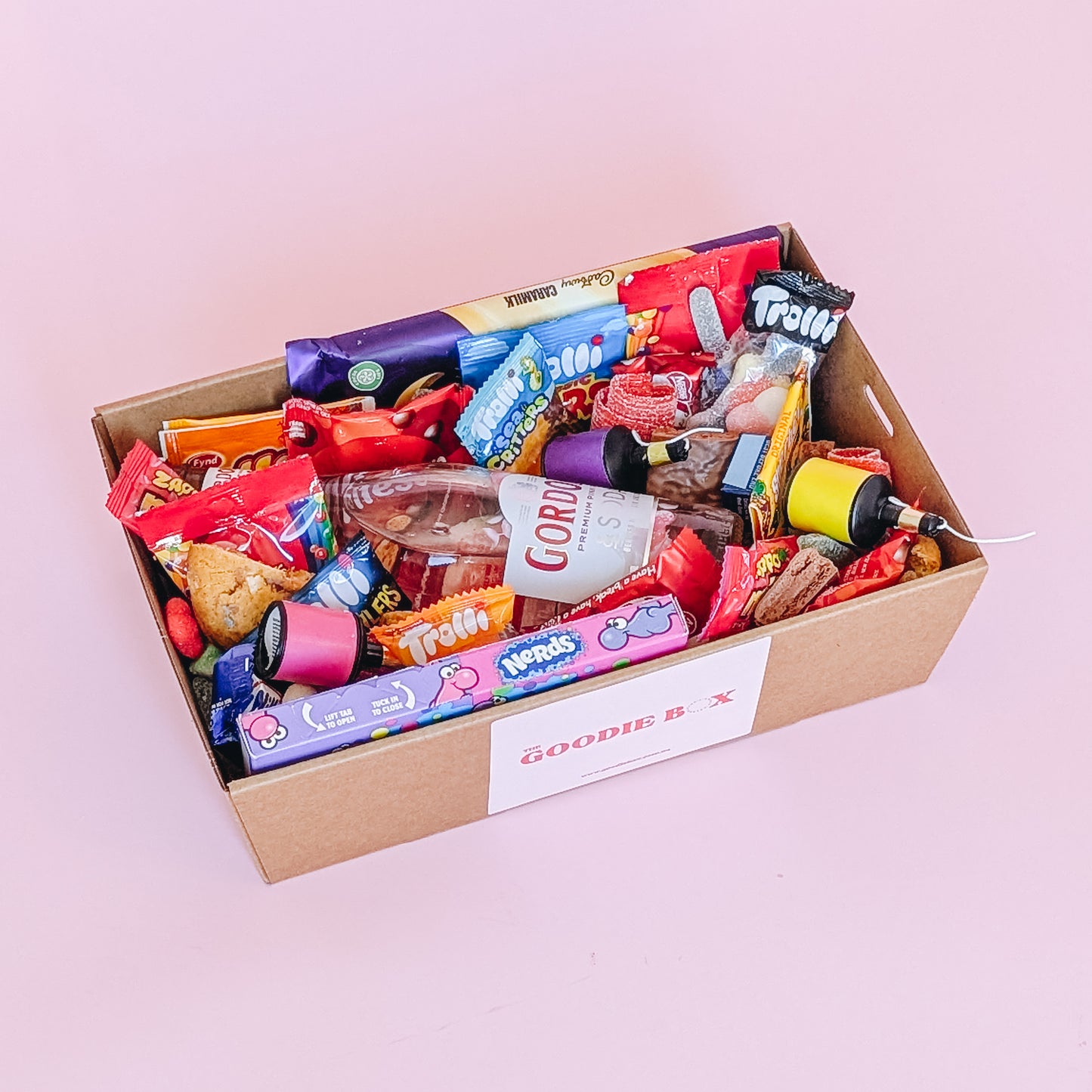Photograph of gift box filled with Gordon's pink gin, Nerds, Cadbury CaraMilk, Trolli Lollies and an assortment of mini chocolates and loose cookies and sweets.