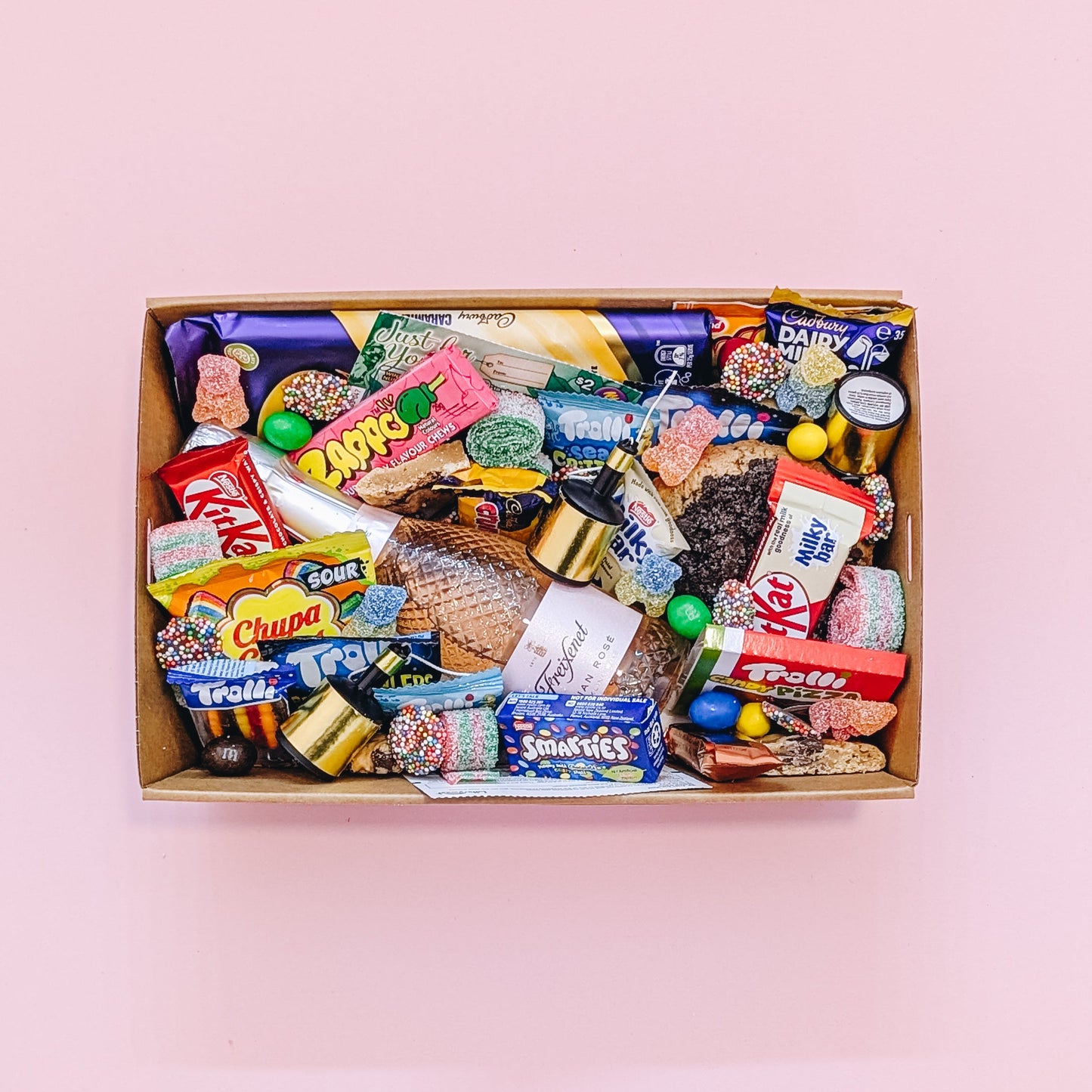 Photograph of dessert birthday box for her featuring sparkling wine, party poppers, chocolates, cookies and lollies. All wrapped in a light pink ribbon with bow.