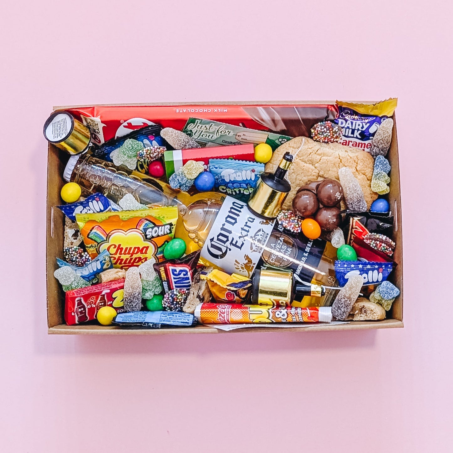 Photograph of gift box filled with Corona, Nerds, Cadbury Dairy Milk, Trolli Lollies and an assortment of mini chocolates and loose cookies and sweets.