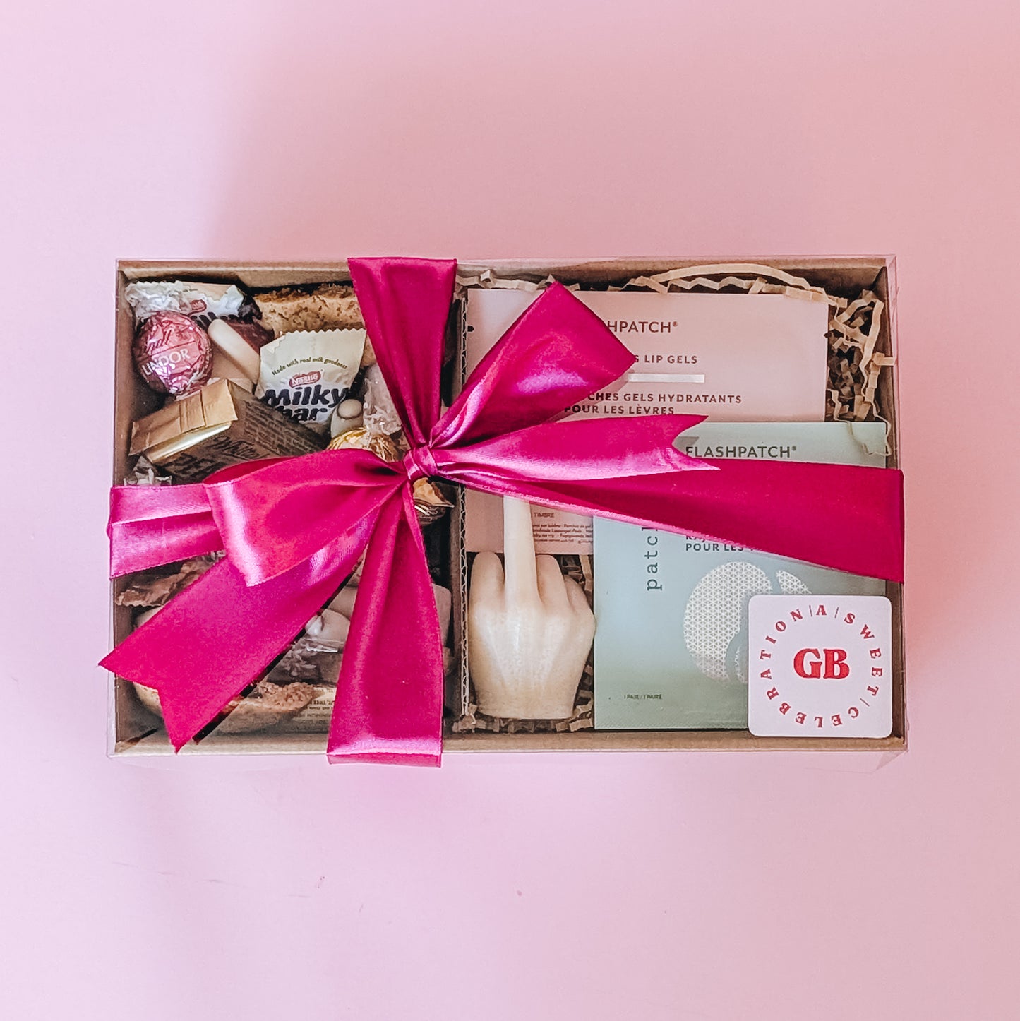 Photograph of the better off without him gift pamper hamper. The gift box is filled with a patchology eye and lip mask, a rude finger candle and an assortment of chocolate, lollies, and cookies. There is a bright pink satin ribbon tied in a bow.