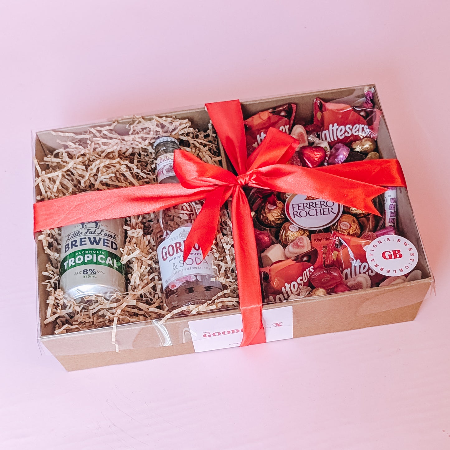photograph of valenitne's romantic gift hamper. It includes a can of cider, a pink gin, and an assortment of chocolates and lollies including: a ferrero Rocher heart, maltesers, swizzels love hearts and love themed sweets. Tied in a bow with a red silk ribbon.