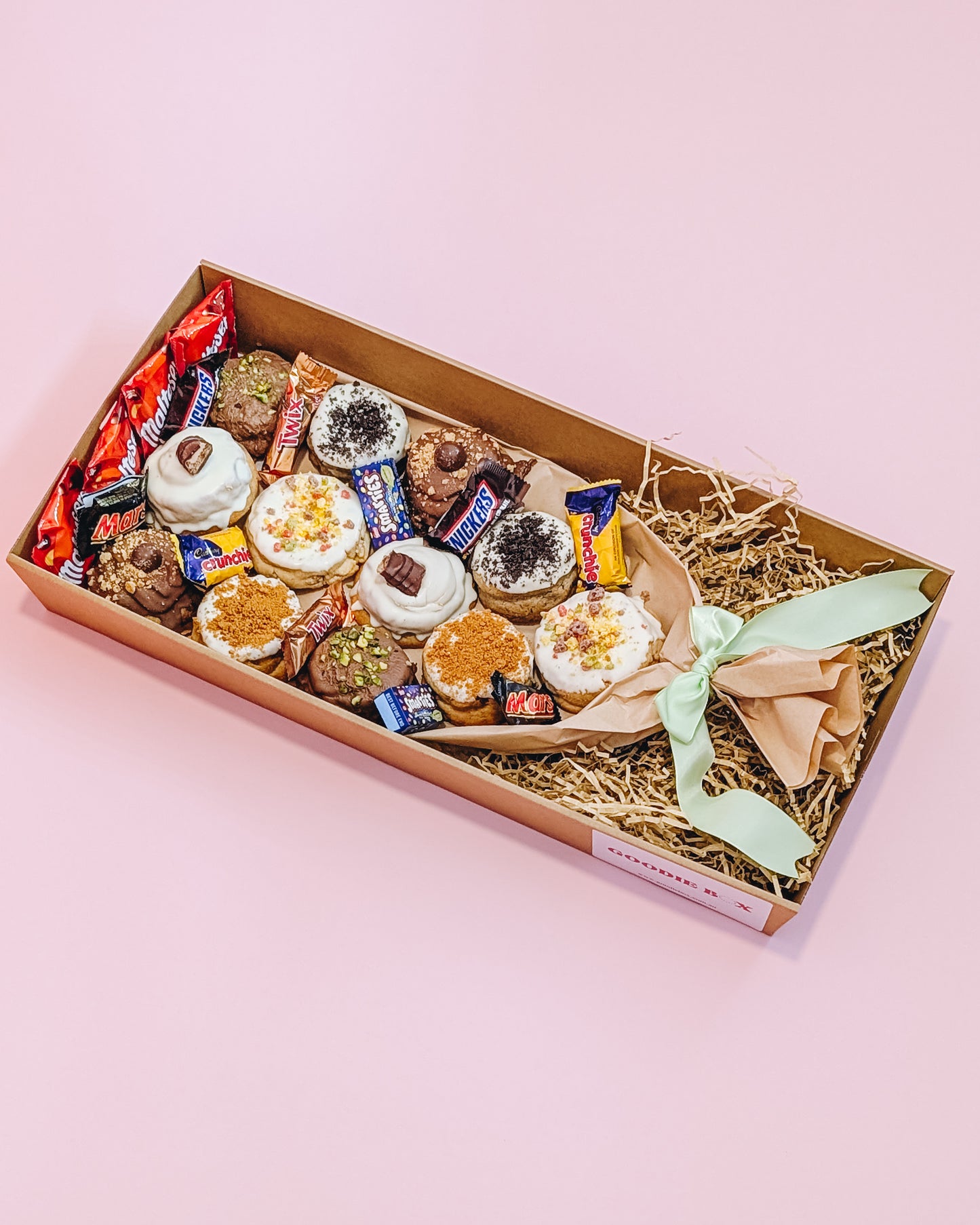 Box of assorted cookies with a decorative bow on a pink background