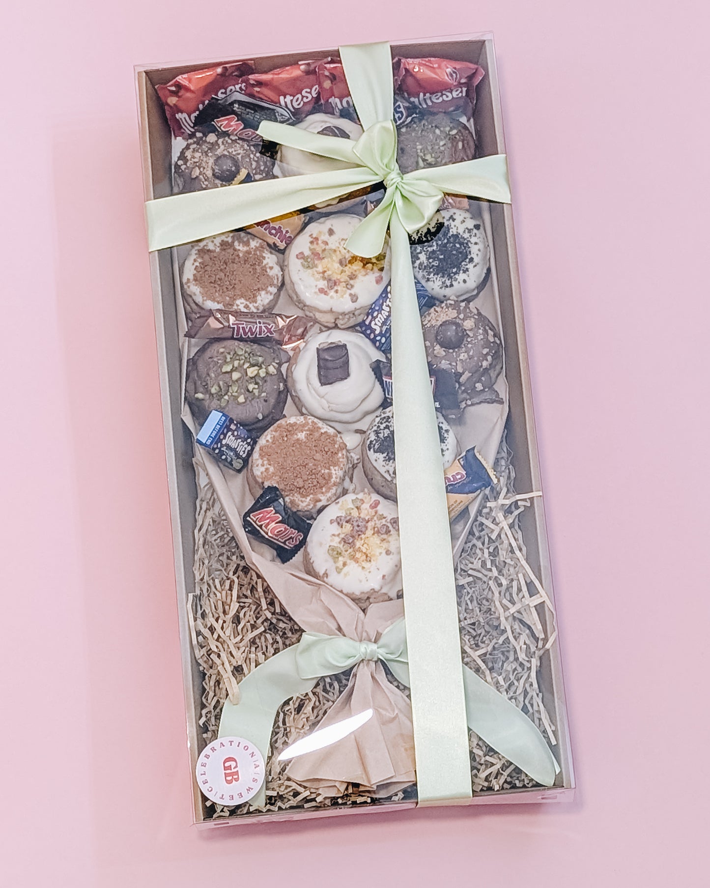 Gift box with assorted cookies and chocolates and a ribbon on a pink background