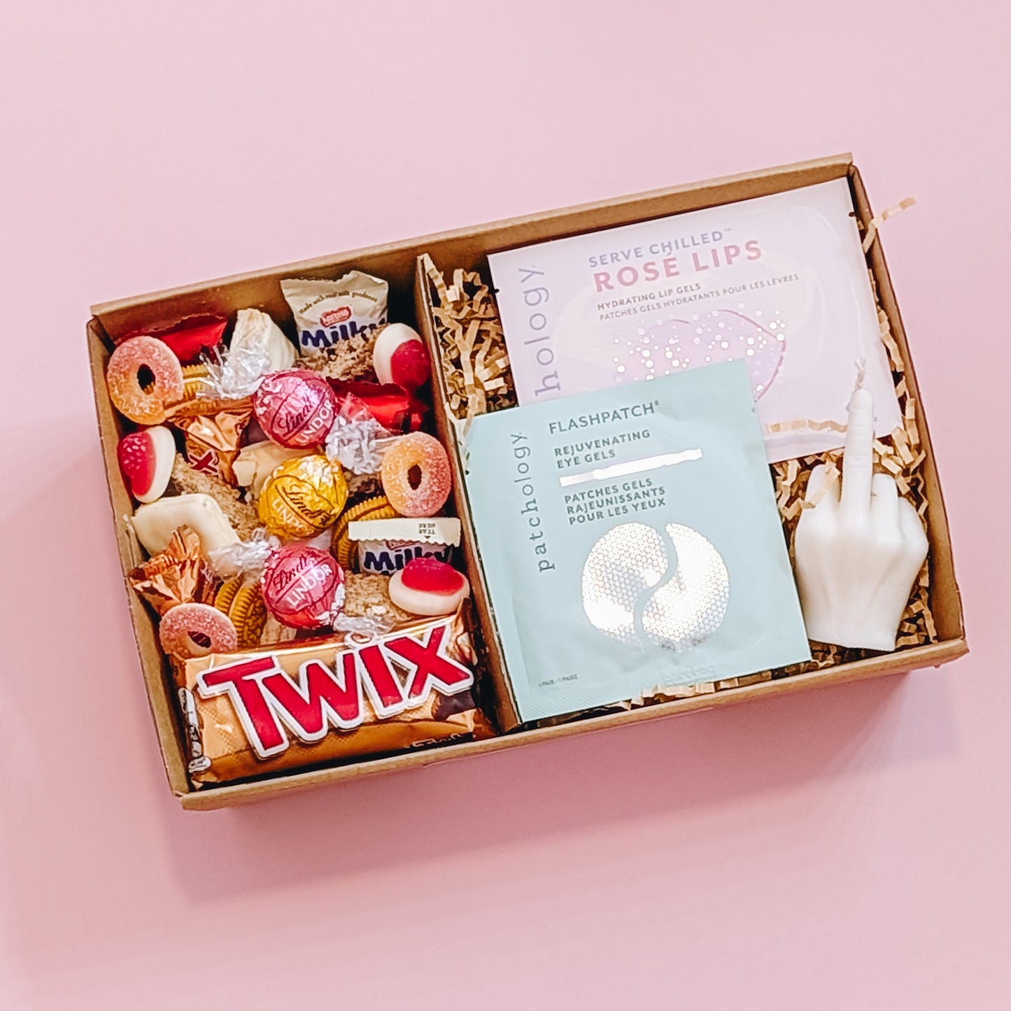 Photograph of the better off without him gift pamper hamper from above. The gift box is filled with a patchology eye and lip mask, a rude finger candle and an assortment of pink and gold chocolate, lollies, and cookies.