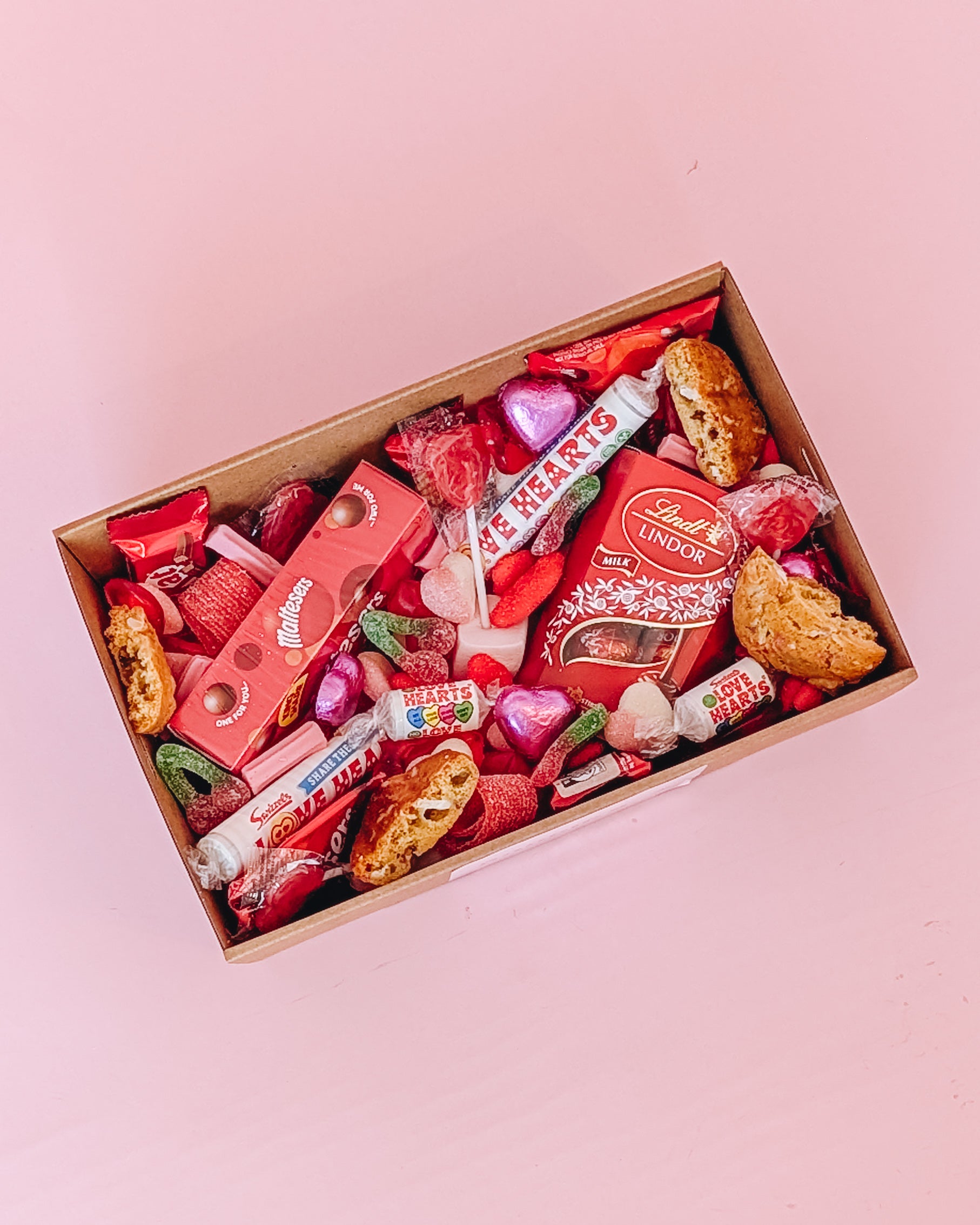 Photograph of Galentines gift hamper ariel view. The dessert box is filled with and assortment of valentines themed chocolates, cookies and lollies.