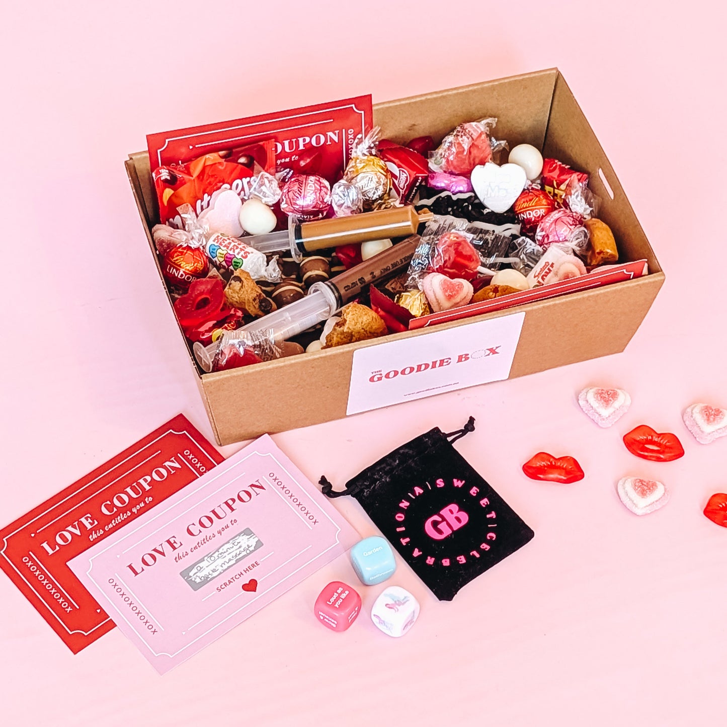 Photograph of valentines gift hamper featuring an assortment of treats including two donuts, lindt chocolates, cookies, nutella and biscoff syringes, love coupons and a black velvet pouch containing dirty dice.