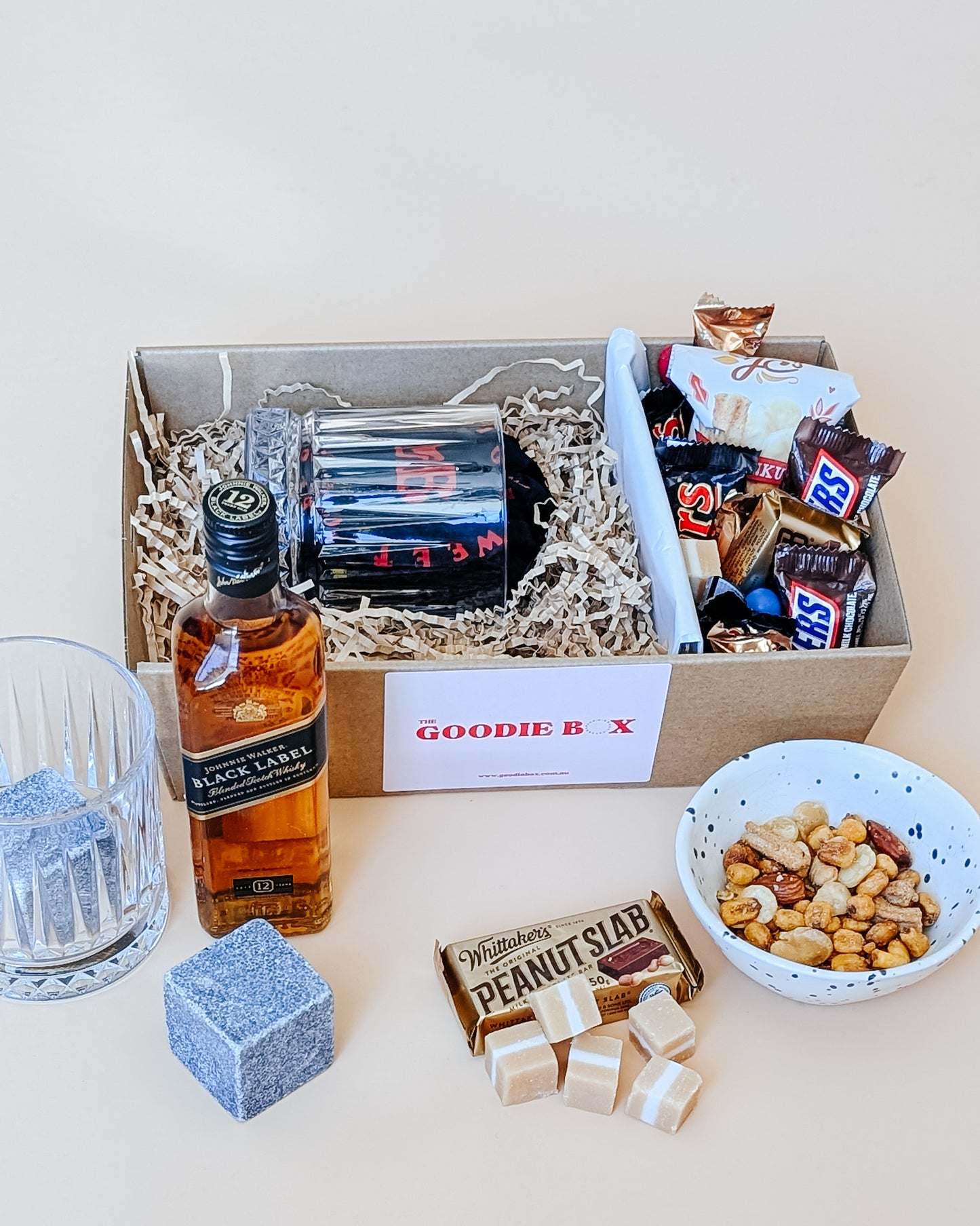 Photograph of whisky gift set for him. The gift hamper is filled with a bottle of Johnny Walker whisky, a whisky glass and a ice cube. The other half is filled with chocolates, nuts and fudge.
