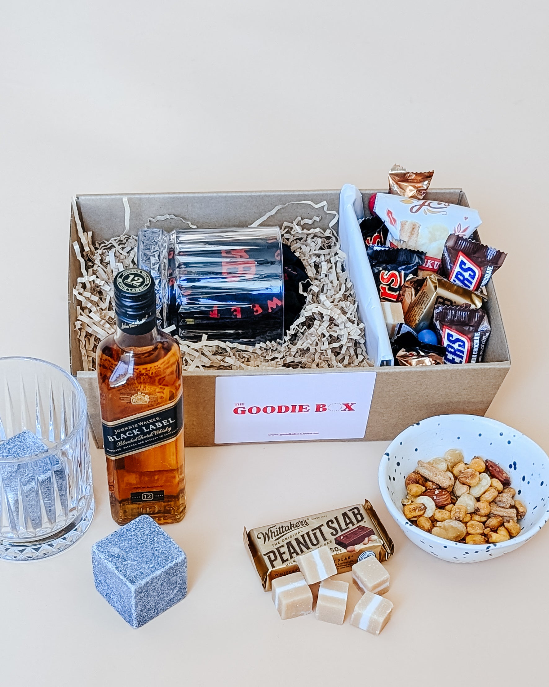 Photograph of whisky gift set for him. The gift hamper is filled with a bottle of Johnny Walker whisky, a whisky glass and a ice cube. The other half is filled with chocolates, nuts and fudge.