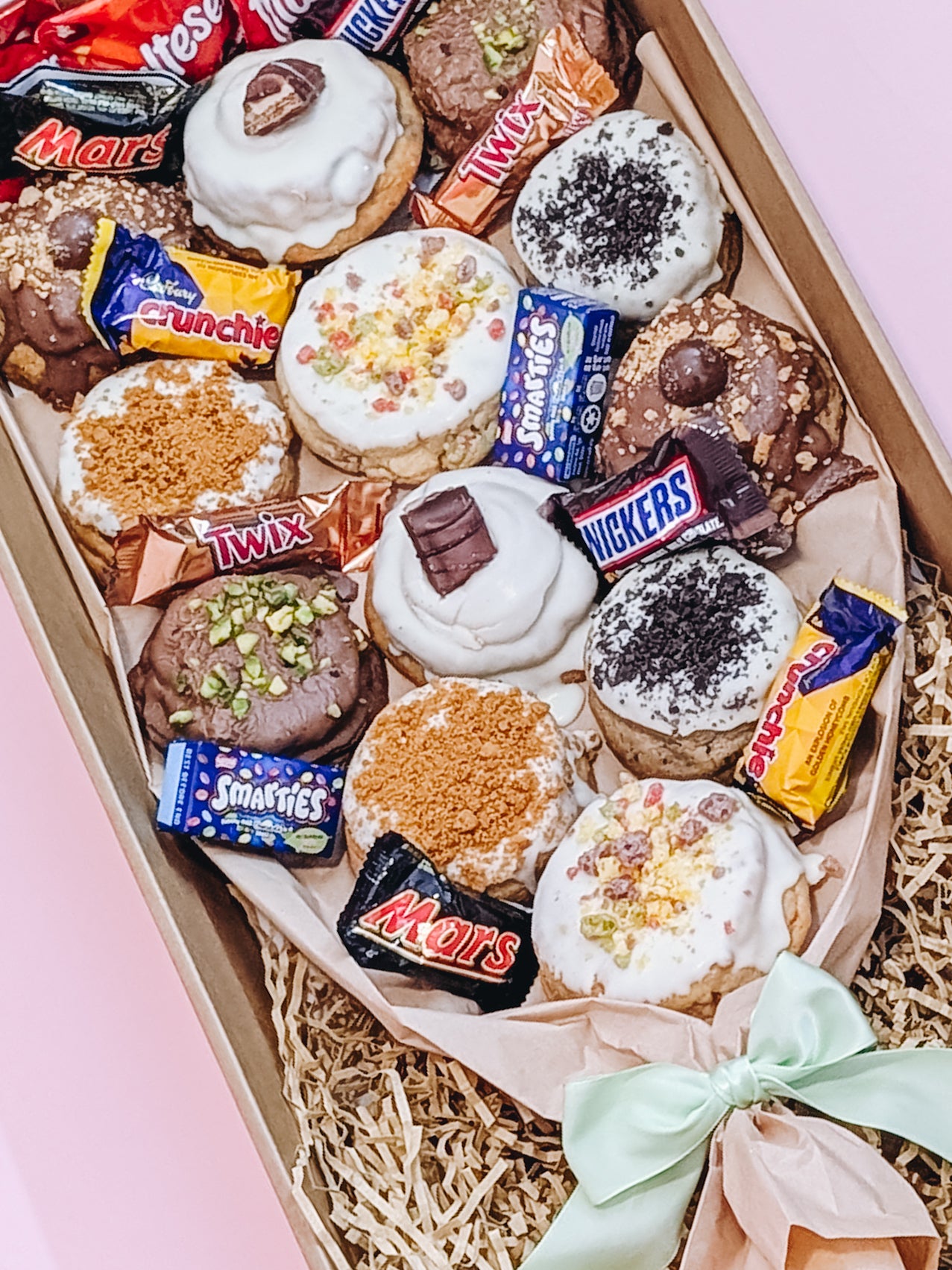 Box of assorted cookies with candy bars on a pink background