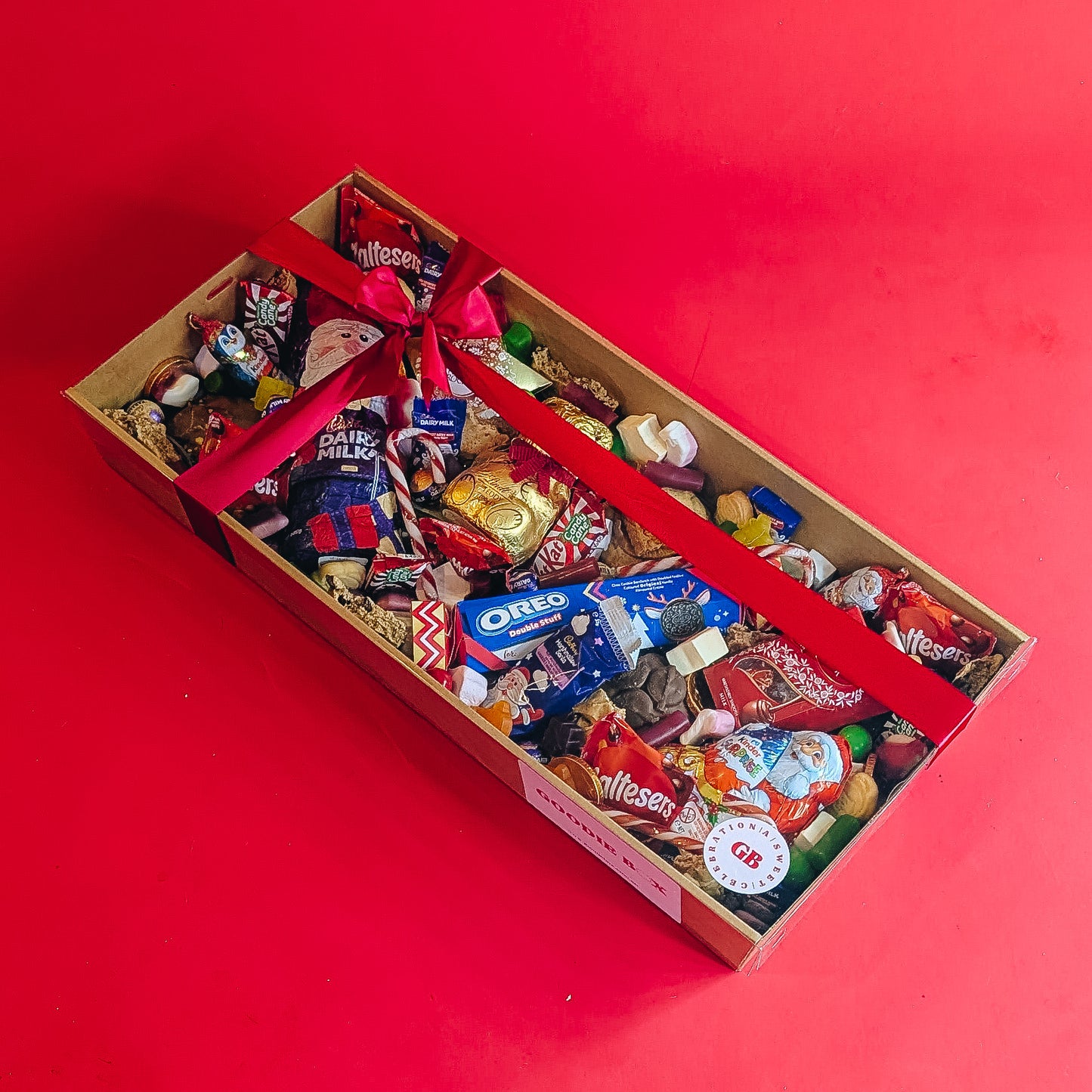 Box of assorted christmas chocolates and candies with a red ribbon on a red background