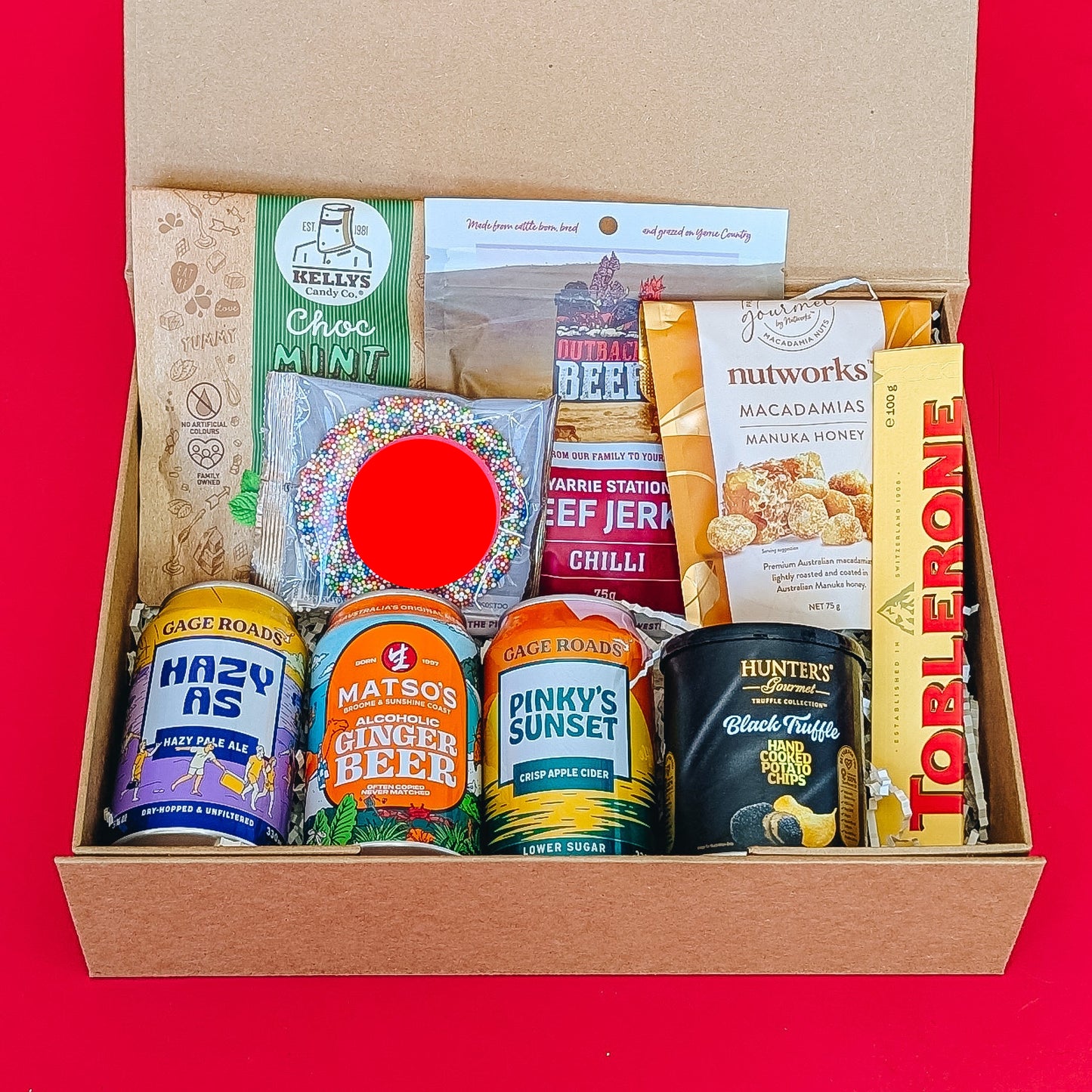 gift hamper with beer, cider and ginger beer with chocolates, beef jerky, crisps and nuts on a red background.