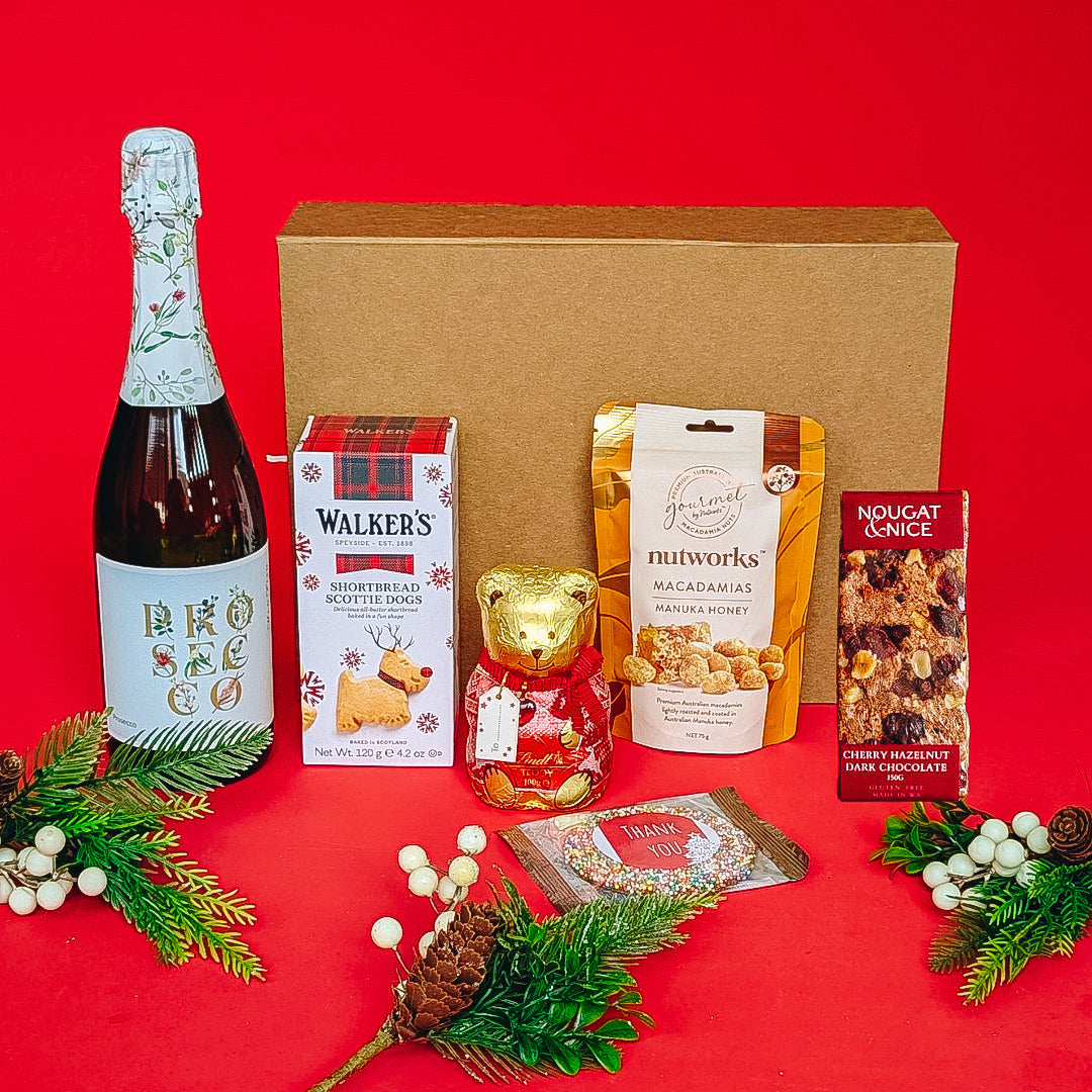 Gift box with bottle of prosecco, buscuits, lindt chocolate and treats on a red background.