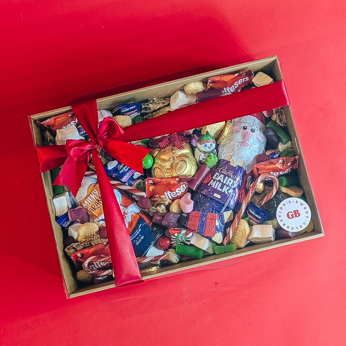 Box of assorted christmas candy with a red ribbon on a red background