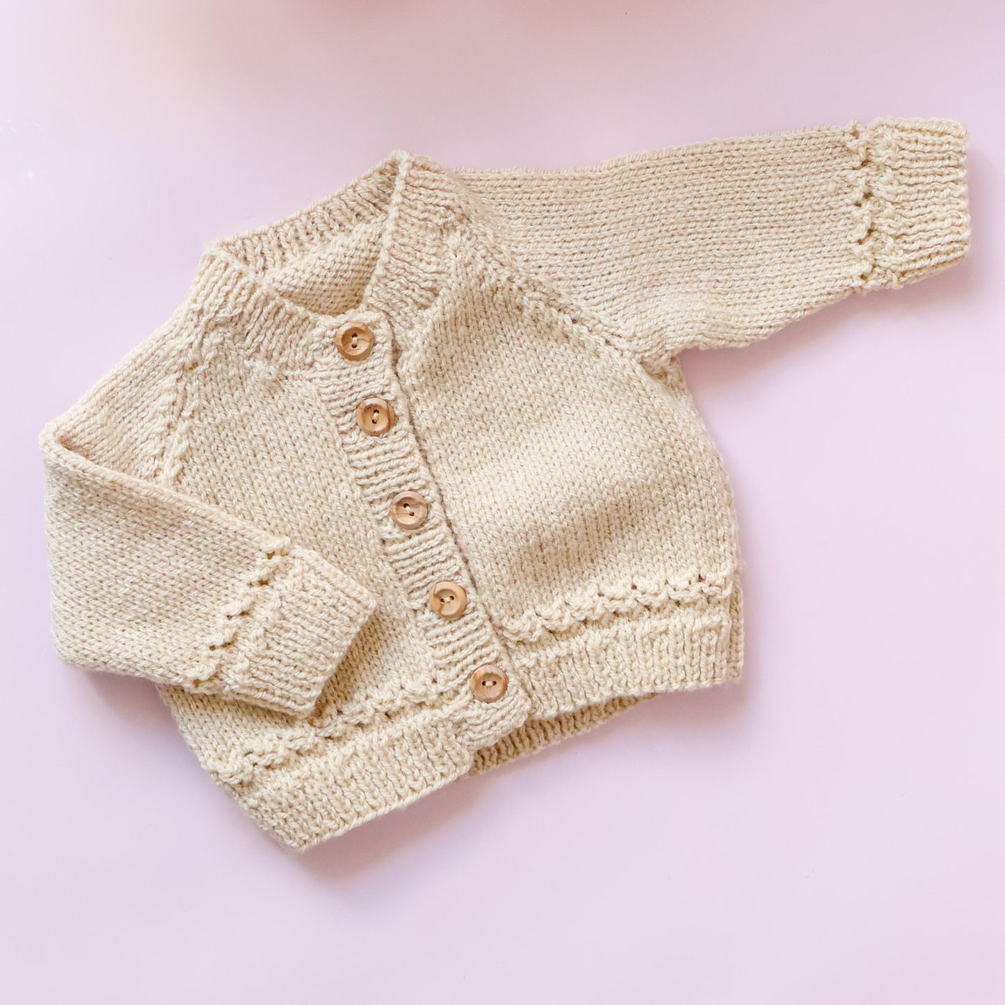 Knitted baby cardigan with buttons on a pink background