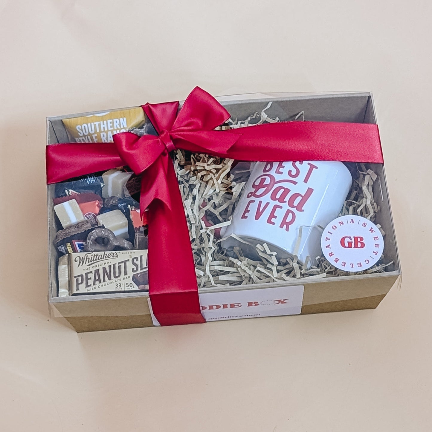 Gift box with a mug, snacks, and a red ribbon on a light background
