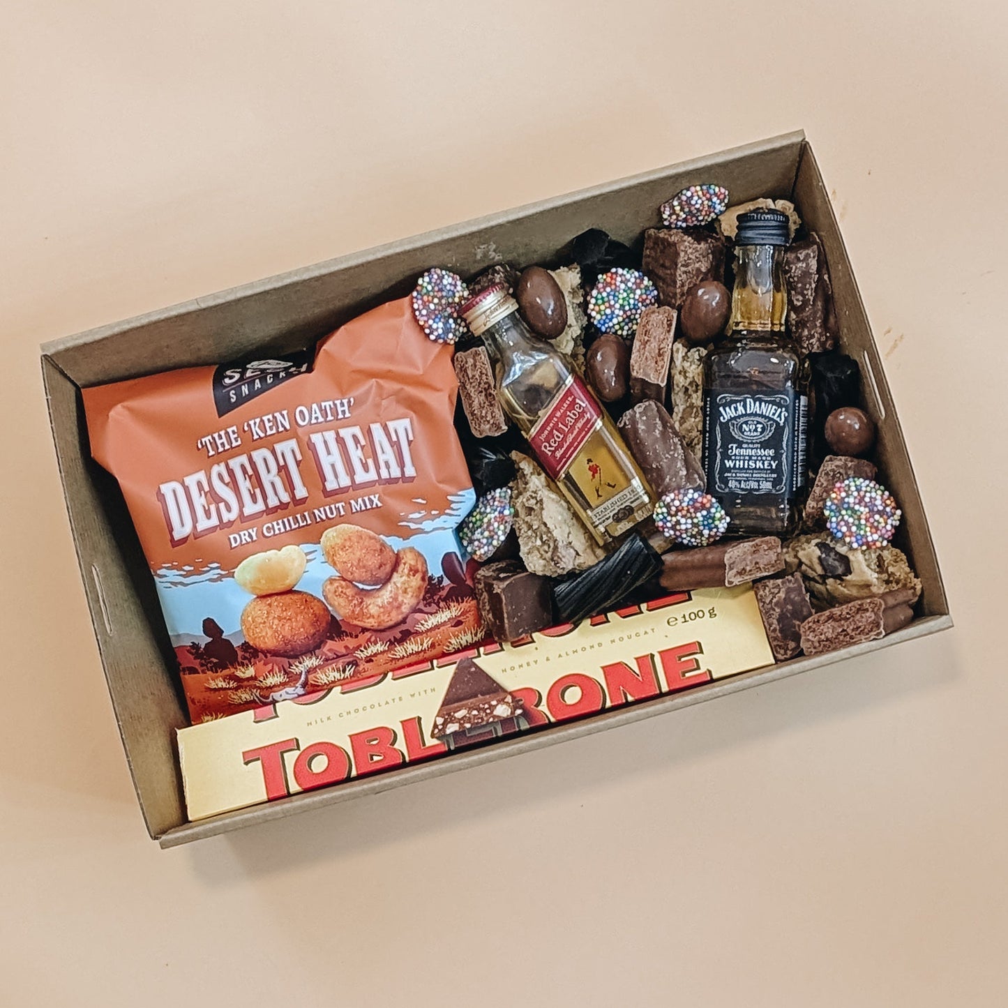 Gift box with snacks, candies, and a bottle of Jack Daniel's on a beige background