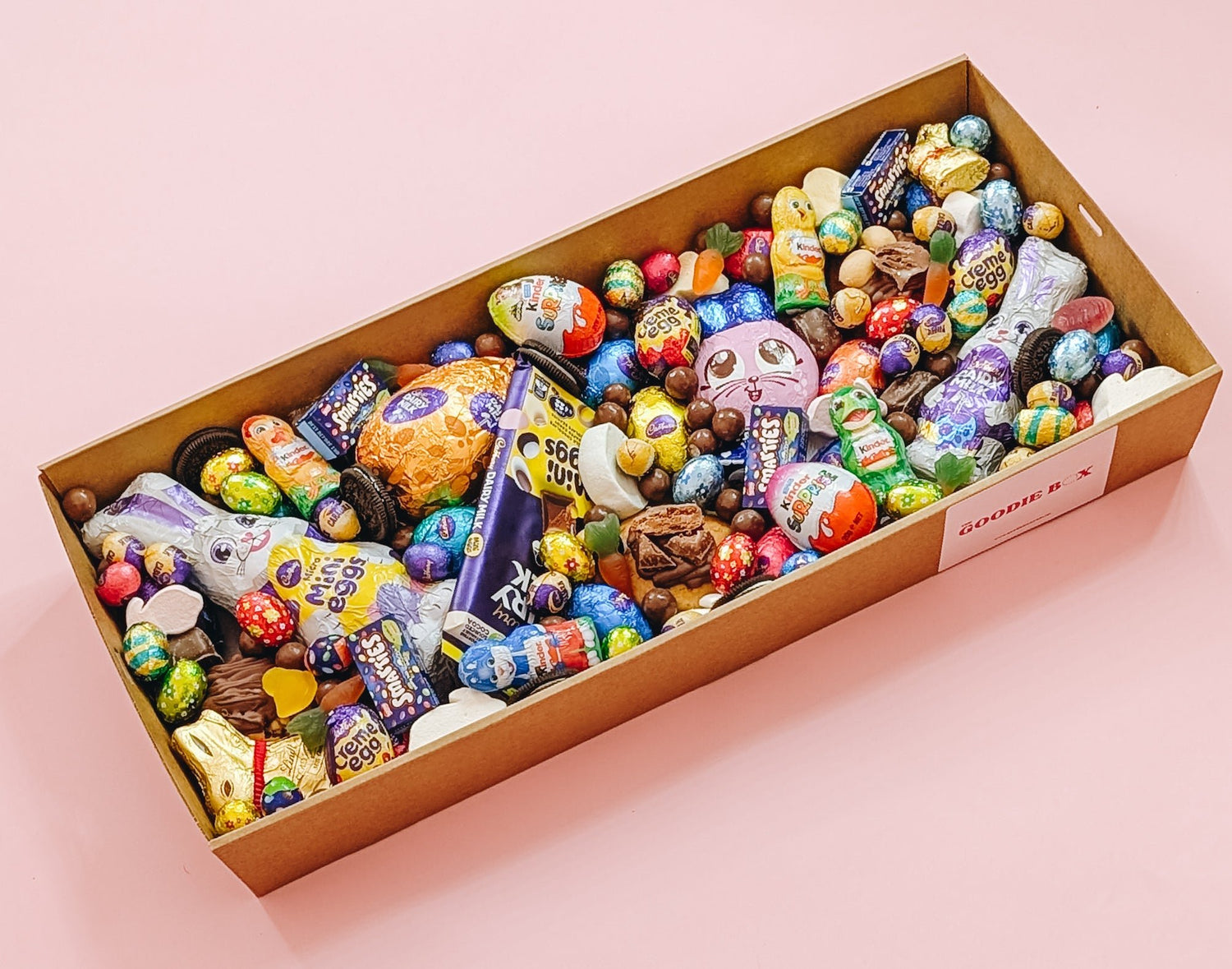 A box of assorted Easter dessert items including chocolates, eggs, and other confectionery treats, presented on a pink background.