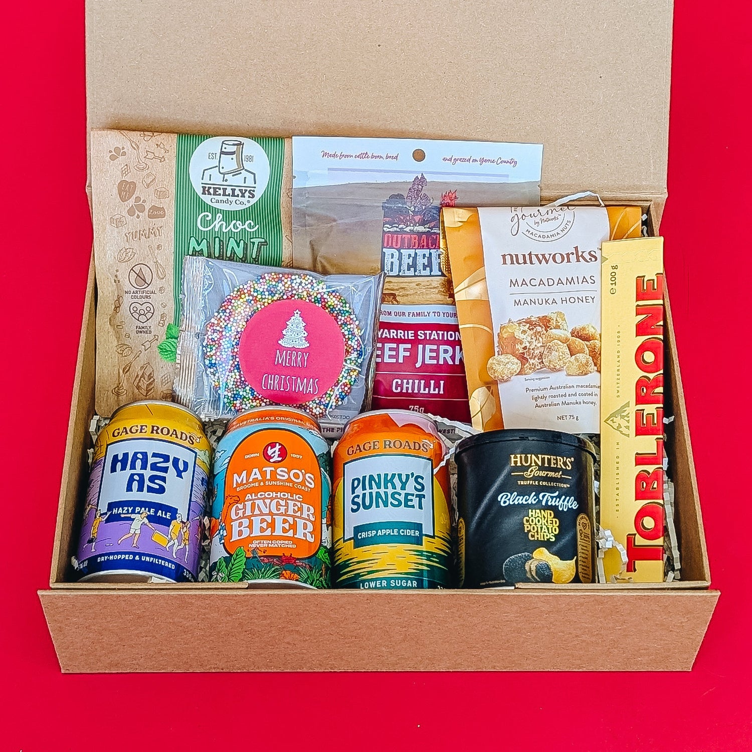 A gift hamper filled with chocolate, fudge, beef jerky, nuts and craft beer and cider on a red background