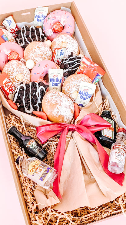Photograph of a dessert box donut bouquet. It is filled with twelve donuts that are different flavours including pink icing sprinkles, chocolate oreo, lemon curd and jam. The box has mini chocolates and sweets along with 4 x miniature alcohols.