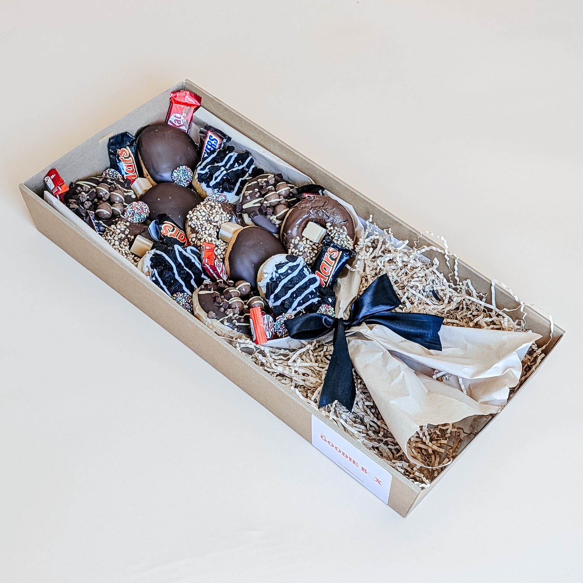Photograph of a box of donuts arranged in a bouquet style. The box also contains an assortment of fun size chocolates and lollies.