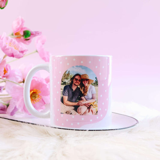 Pink polka dot mug with a custom personalised photo on a pink surface with flowers.