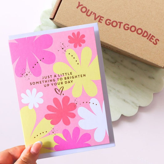Floral card with colorful flowers and text, held by a hand, next to a box labeled 'YOU'VE GOT GOODIES'.