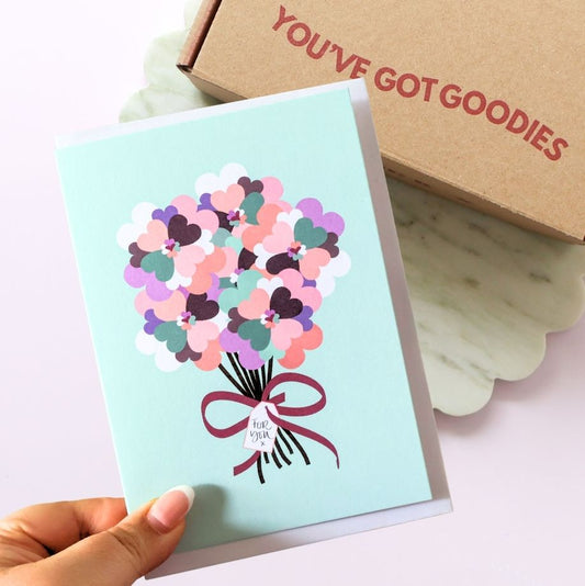 Greeting card with colorful heart bouquet design held by a hand, next to a box labeled 'YOU'VE GOT GOODIES'.