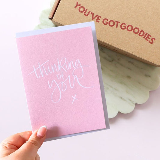 Pink Greeting card reading "thinking of you" with a gift box in the background reading you.ve got goodies