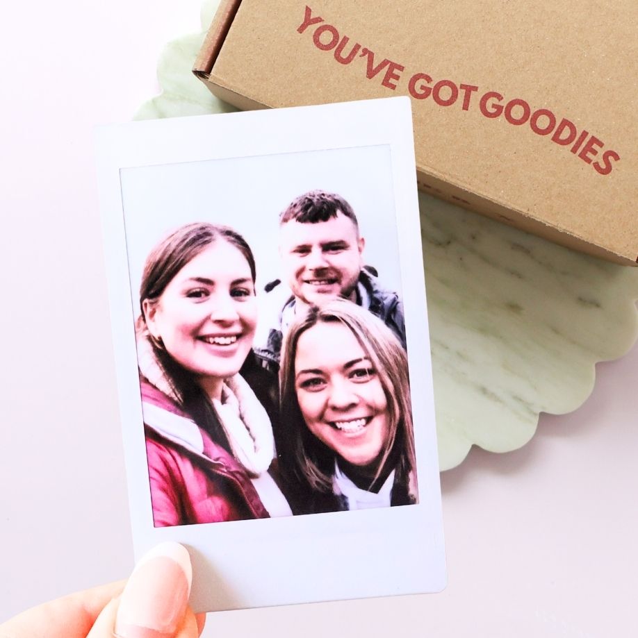 Photo of three people on a card with a brown box labeled 'You've Got Goodies' in the background.