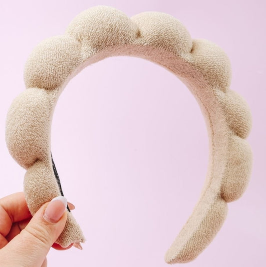 Beige textured headband held by a hand against a pink background