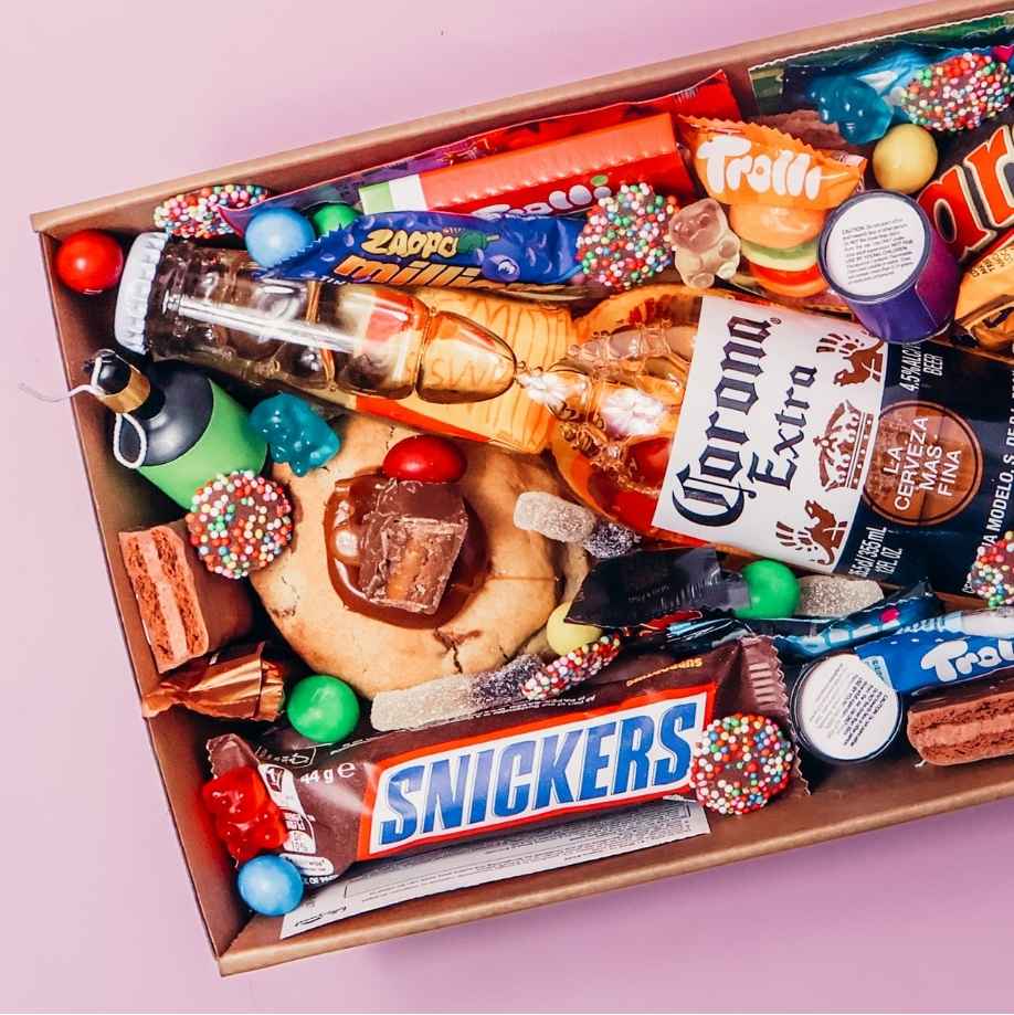 Close up of Goodie Box dessert box for him filled with Corona Extra beer, Snickers bar, Trolli lollies, M&Ms, Mars, loaded cookie and Nutella syringe