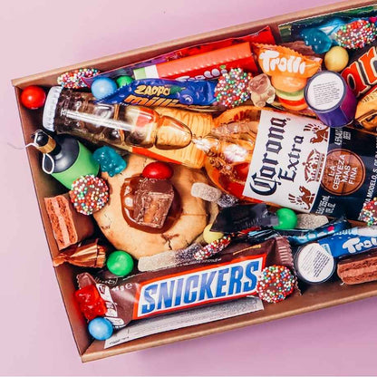 Close up of Goodie Box dessert box for him filled with Corona Extra beer, Snickers bar, Trolli lollies, M&Ms, Mars, loaded cookie and Nutella syringe
