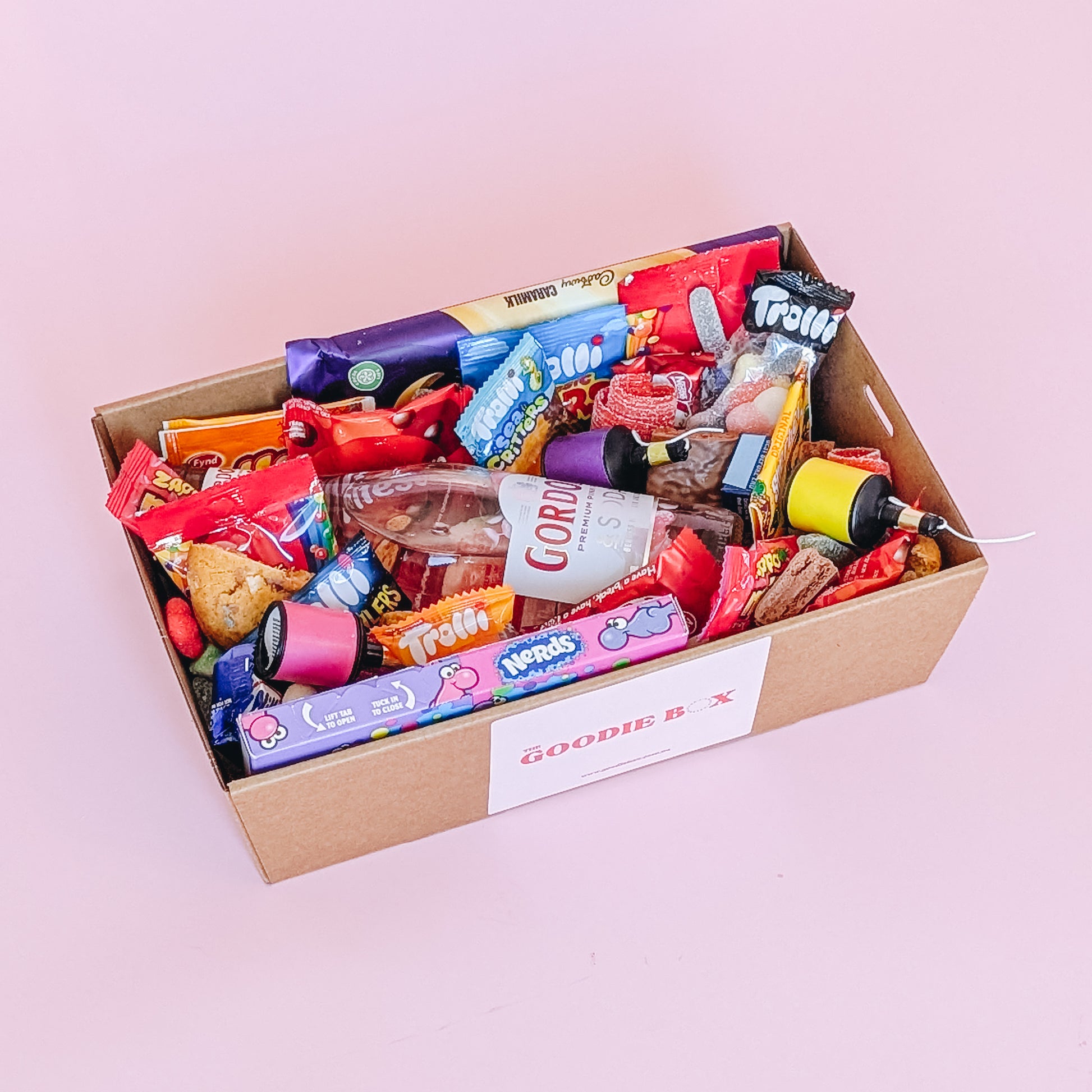 Photograph of gift box filled with Gordon's pink gin, Nerds, Cadbury CaraMilk, Trolli Lollies and an assortment of mini chocolates and loose cookies and sweets. 