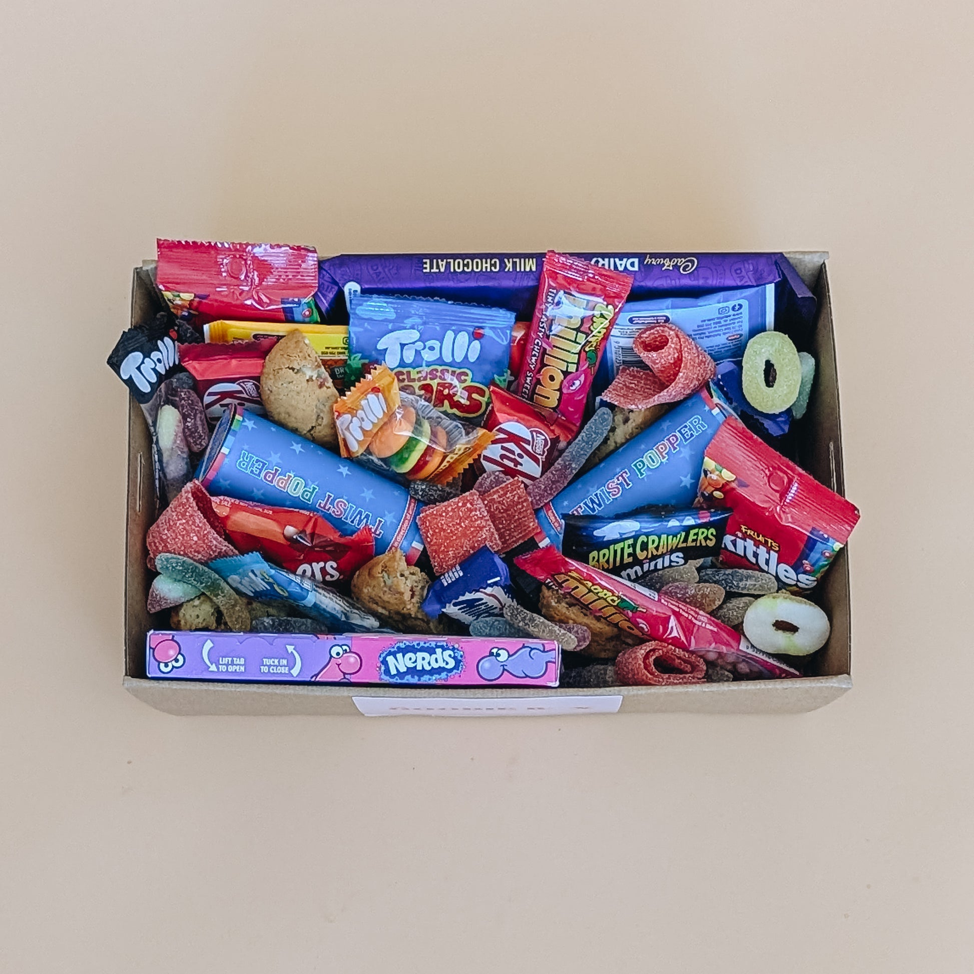 Photograph of birthday dessert gift box. It is filled with chocolate bars, a selection of lollies, cookies and party poppers.