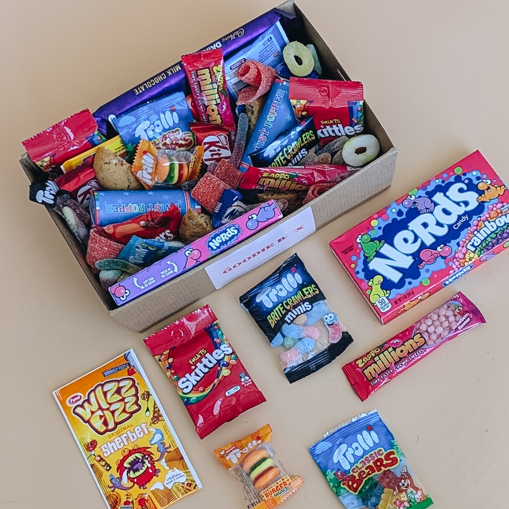 Photograph of birthday dessert gift box. It is filled with chocolate bars, a selection of lollies, cookies and party poppers. There are sweets scattered around like Wizz Fizz, Skittles and Trolli Burgers.