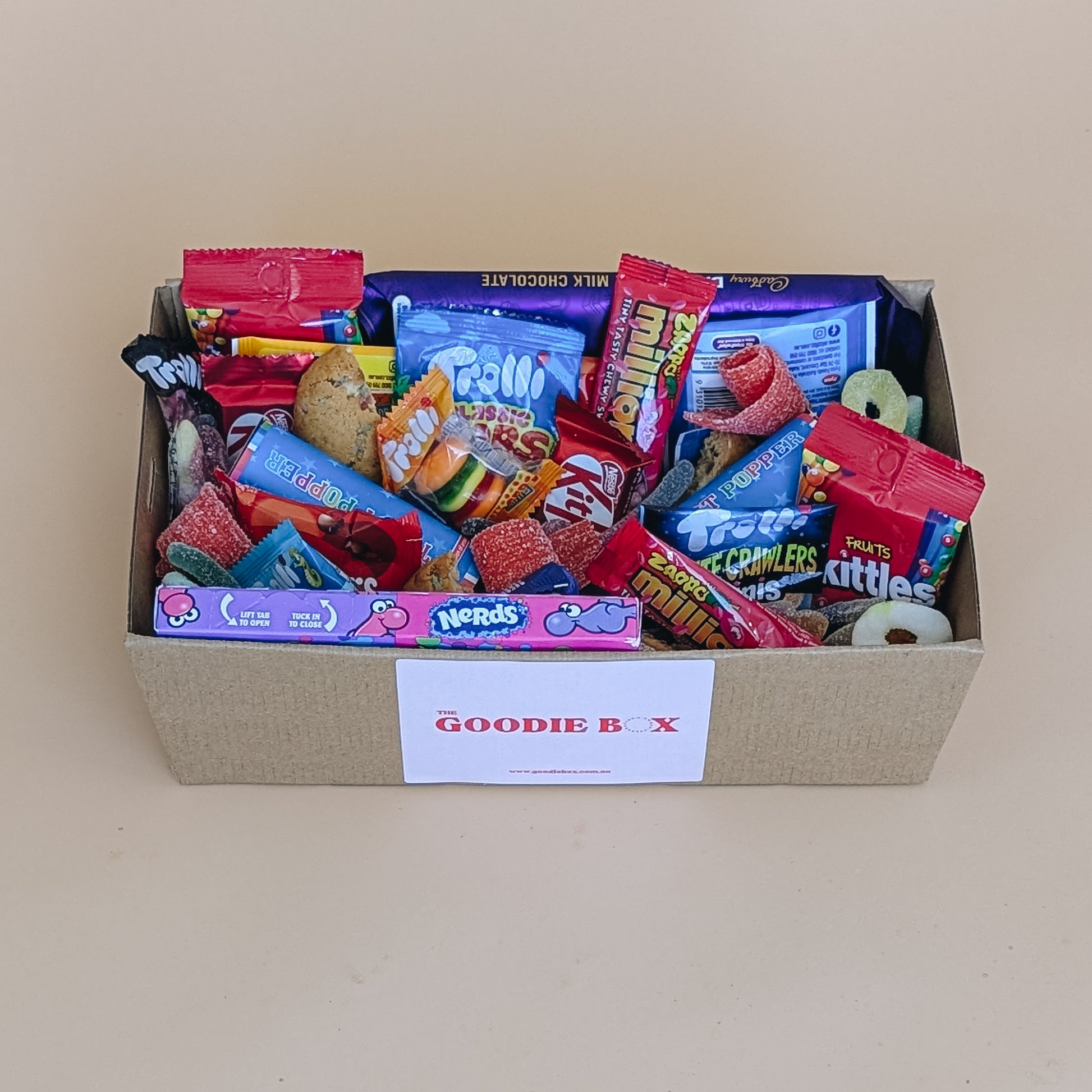 Photograph of birthday dessert gift box. It is filled with chocolate bars, a selection of Trolli lollies, Nerds, cookies and party poppers.