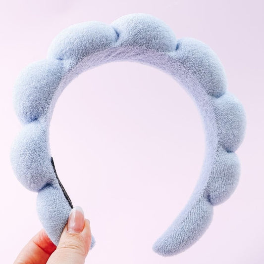 Light blue headband held by a hand against a light pink background
