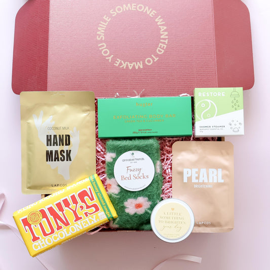 Pamper gift box showing Huxter body bar shower steamer fuzzy bed socks Lapcos Pearl face mask and Brighten Your Day candle