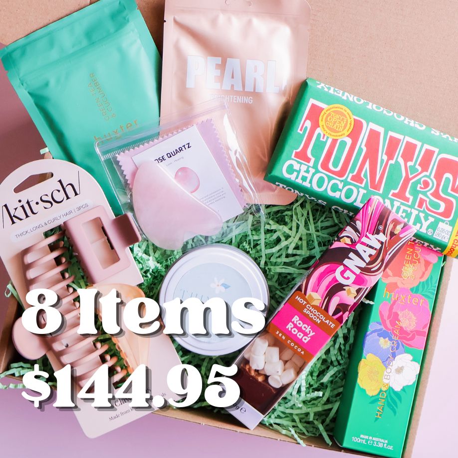 Collection of beauty and lifestyle products including a box of Tony's Chocolonely, Kit-sch hair clips, and other items on a pink background.