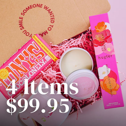 open gift box displaying items including a candle a Huxter hand and body cream, a pink mug and block of Tony's Chocolonely chocolate in a box with pink shredded paper and gift box reading "someone wanted to make you smile".