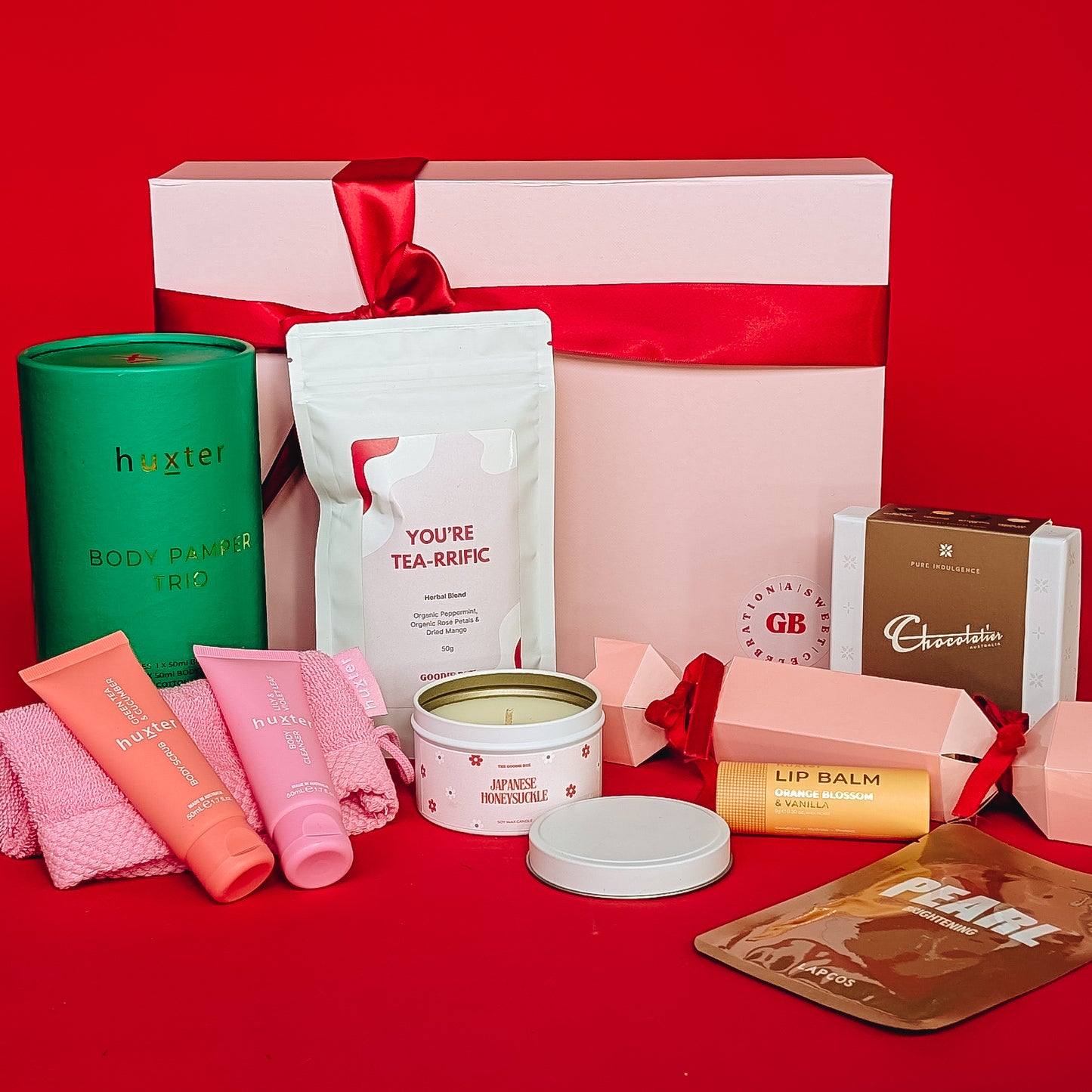 Gift set with various items including a candle, tea, and chocolate on a red background