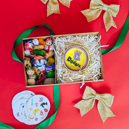Gift box with toys and a 'Dobble' game on a red background with gold bows.